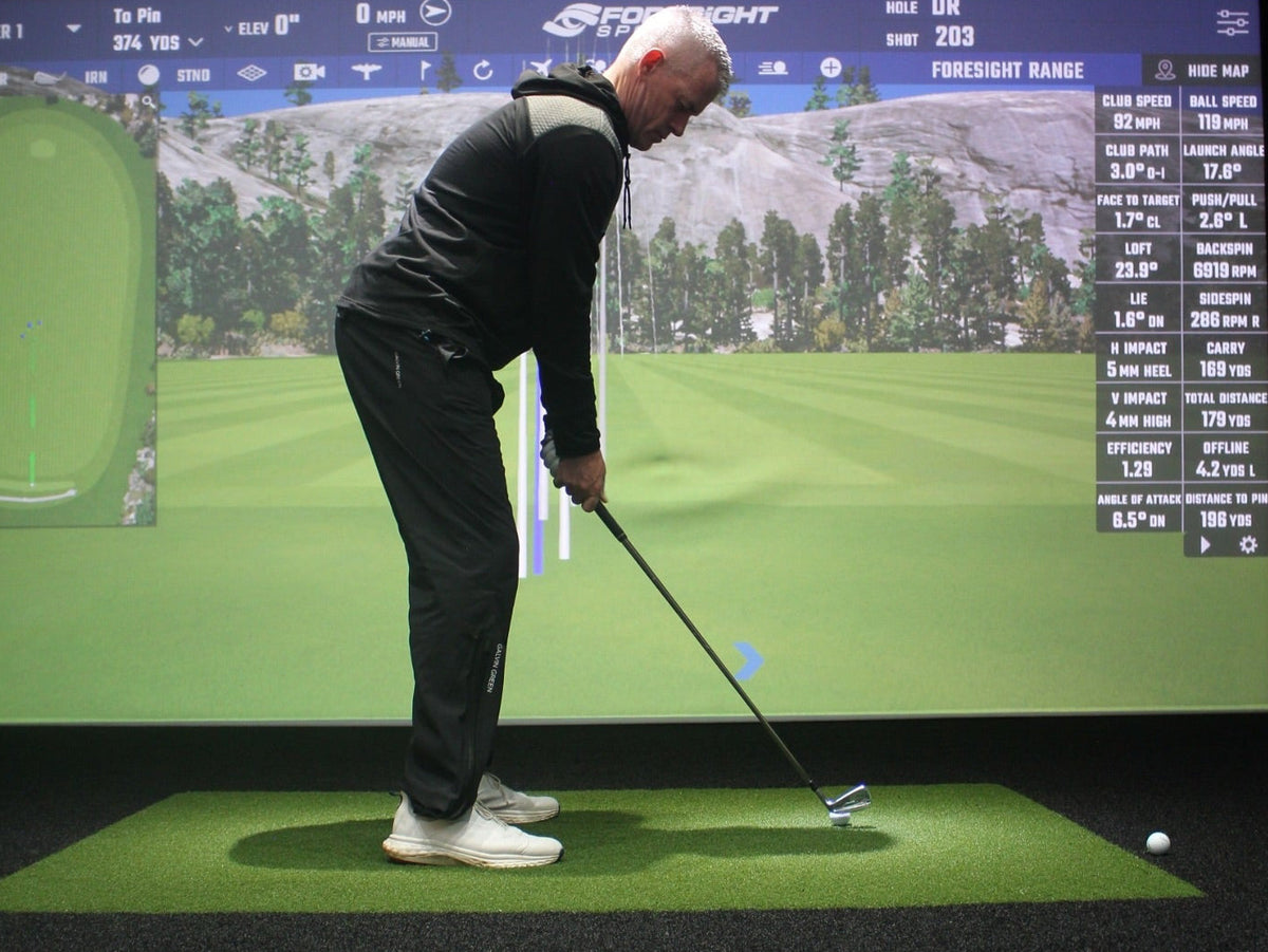 Person practicing golf swings in a simulator with digital display